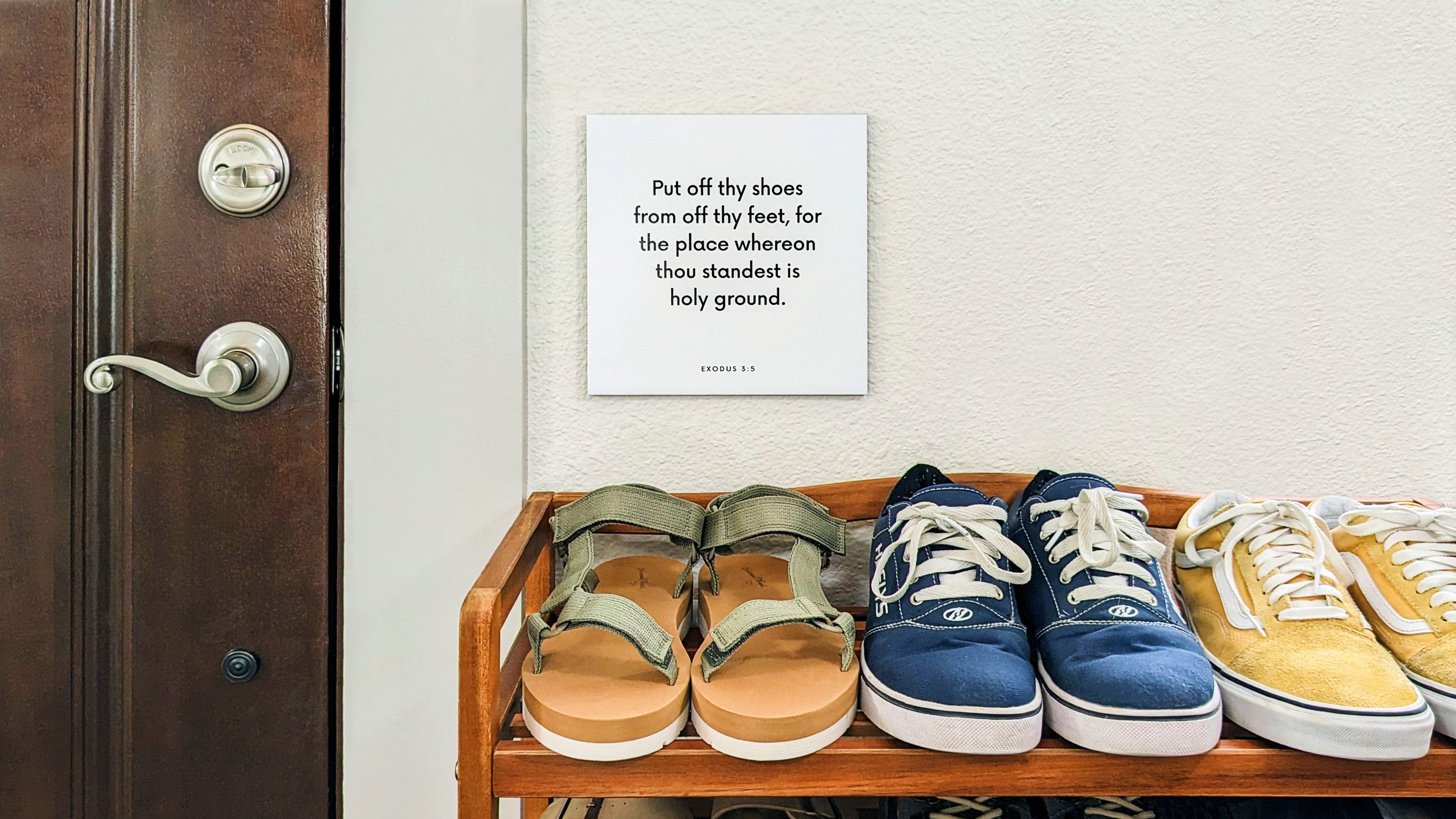 Shoe rack with a scripture tile on the wall next to it